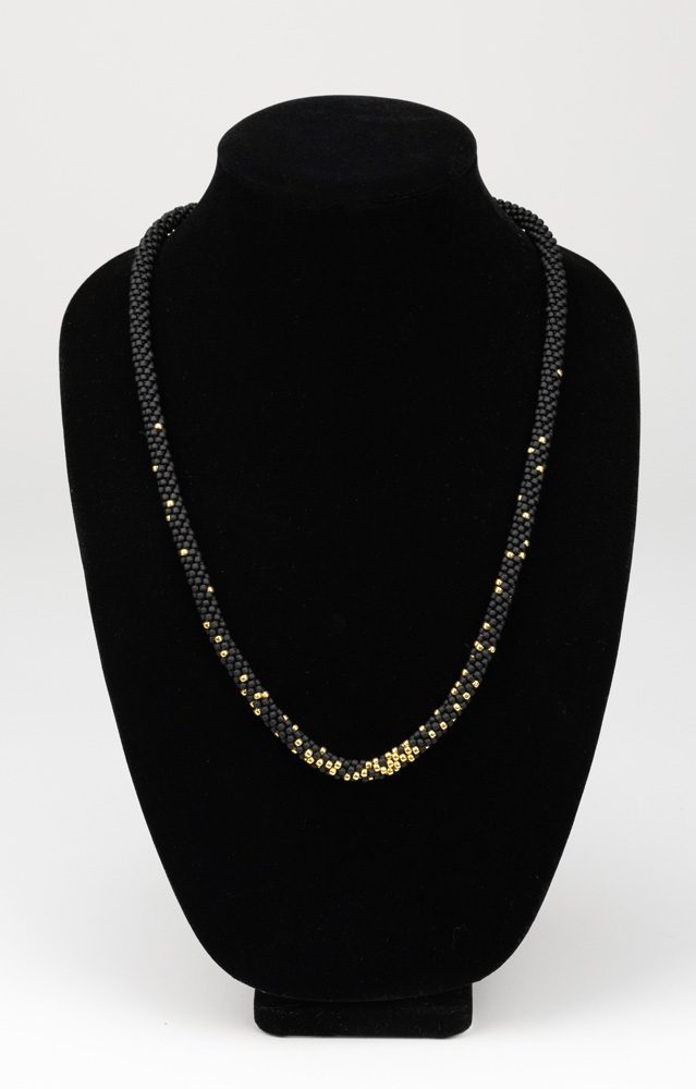 A black and gold necklace is displayed on a black velvet display.