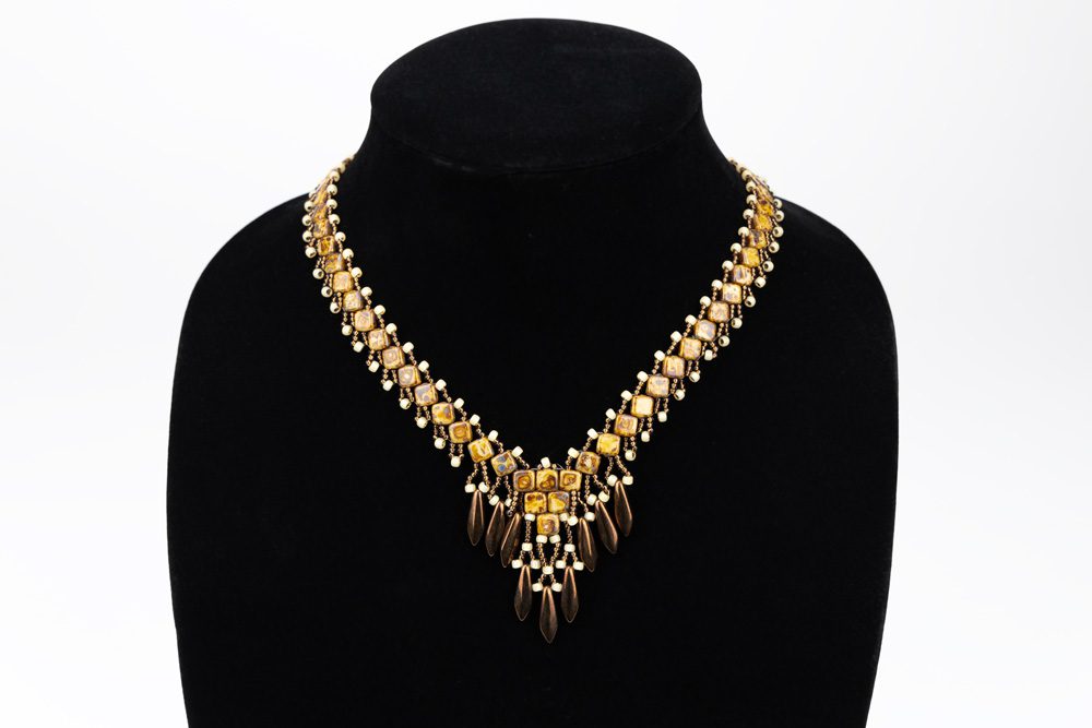 A black mannequin wearing a necklace with gold and white beads.