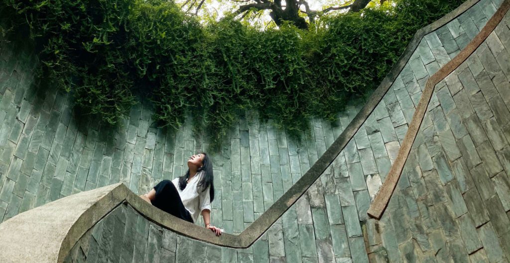 A woman is sitting on the ground in front of a wall.